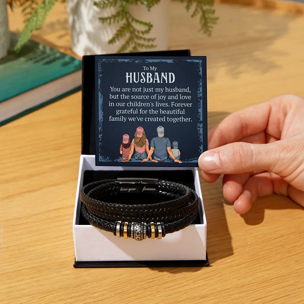 Black leather bracelets in a box with a personalized card held by a hand on a wooden surface.